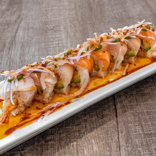 Wazabi Sushi's long plate of sushi rolls, topped with salmon, avocado, onions, and sauce.