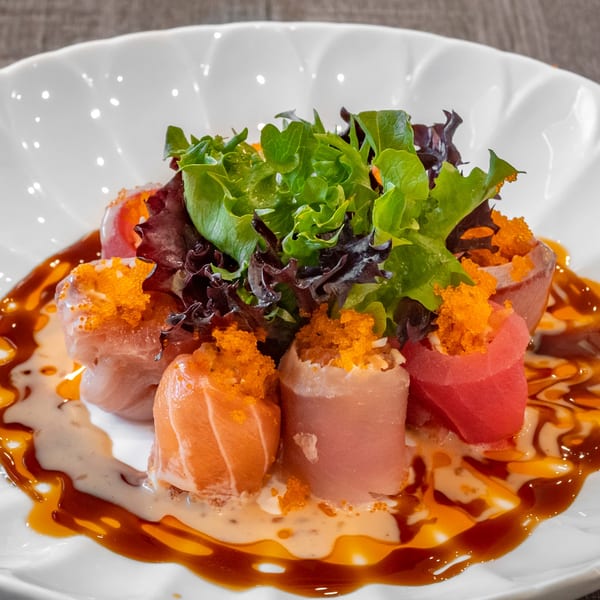 Wazabi Sushi's colorful sushi rolls with salmon, tuna, tobiko, and greens, drizzled with sauce.