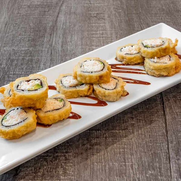 Crispy fried sushi rolls with creamy filling and avocado, drizzled with sauce on a white plate.