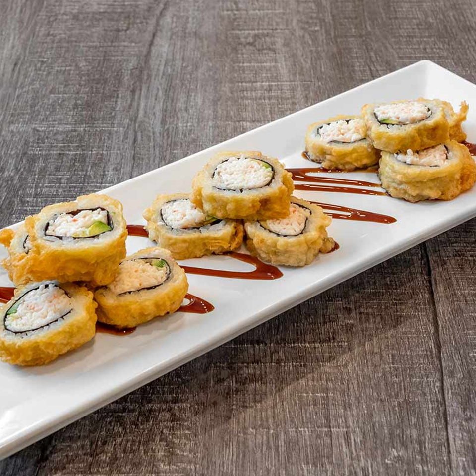 Crispy fried sushi rolls with creamy filling and avocado, drizzled with sauce on a white plate.