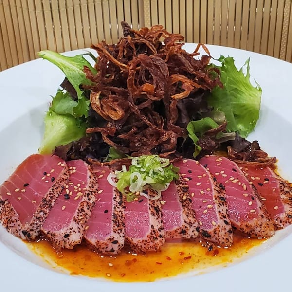 Seared tuna sashimi with sesame seeds, green onions, mixed greens, and crispy fried onions.