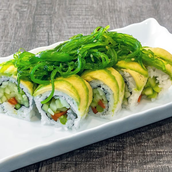 Wazabi Sushi's avocado and vegetable sushi rolls topped with bright green seaweed salad on a white plate.