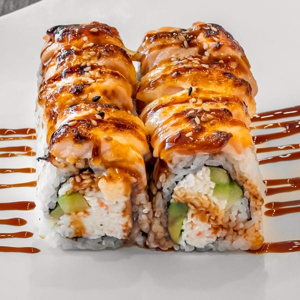 Two sushi rolls with seared salmon, sesame seeds, and a sweet glaze on a white plate.