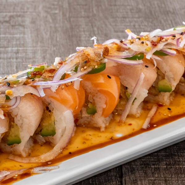 Wazabi Sushi roll with salmon, avocado, and red onion, drizzled with sauce on a white plate.