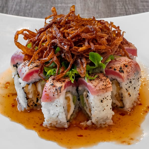 Wazabi Sushi's tuna sushi roll, topped with crispy fried onions, lettuce, and a savory sauce.