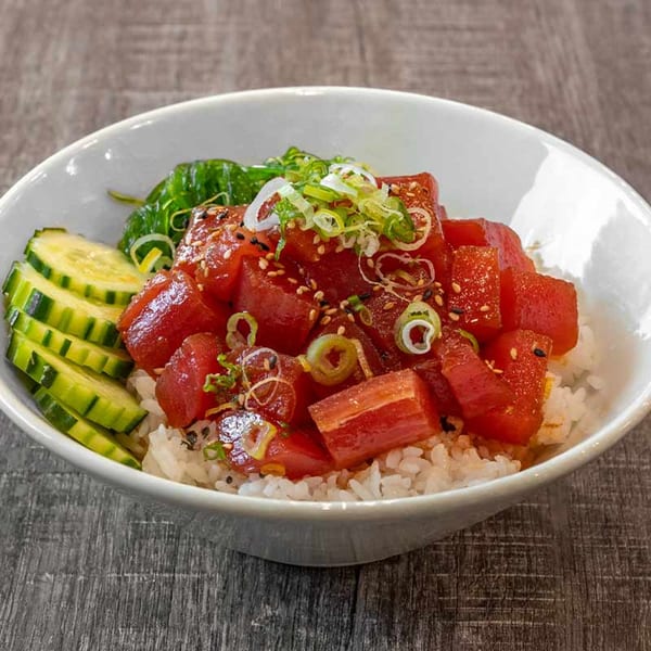 A close-up of a Wazabi Sushi poke bowl with tuna, rice, cucumbers, seaweed, and green onions.
