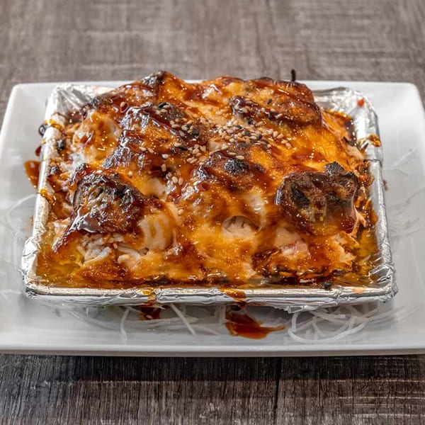 Wazabi Sushi's baked sushi dish, topped with melted cheese, sauce, and sesame seeds in a foil container.