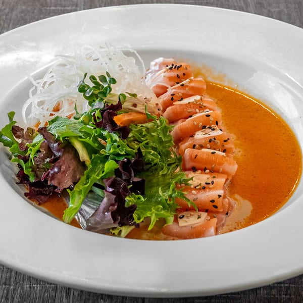 Wazabi Sushi's salmon sashimi with sesame seeds, salad, and white radish in a spicy orange sauce.