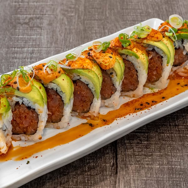 Wazabi Sushi's spicy tuna roll with avocado, orange sauce, and green onions on a white plate.