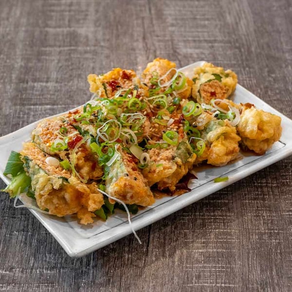 Crispy fried sushi rolls topped with green onions, sesame seeds, and sauce on a white plate.